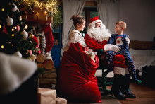 Young Girl And Boy Sitting With Santa, Sack Full Of Presents Beside Him
