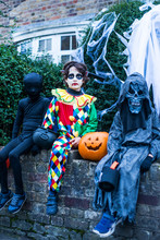 Portrait Of Three Boys In Halloween Costumes, Sitting On Wall