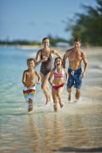 Happy Family Splashing In Shallow Water At A Tropical Beach
