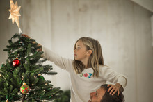 Girl Placing The Star On The Top Of The Christmas Tree With Her Father