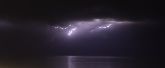 Wall Mural - lightning bolts reflection over the sea. taken during a thunderstorm over the ocean with clouds in the background