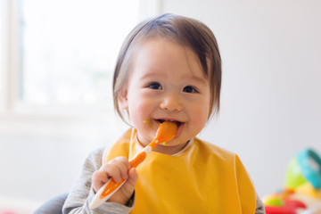 happy little baby boy eating food in his house