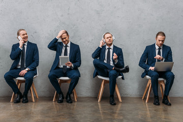 Wall Mural - collage of cloned young businessman sitting on chairs and using gadgets