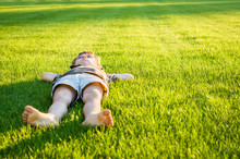 The Boy Lies On A Well-groomed Lawn Illuminated By The Sun's Rays