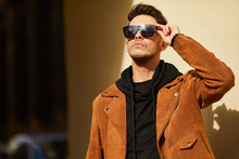 Model Looking Man Stand Near The Wall And Hold His Glasses Towards The Sun Shine