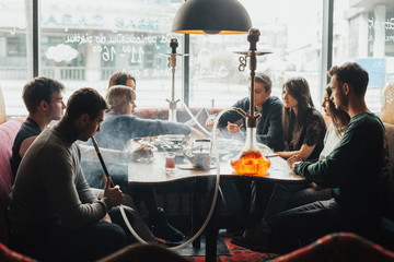 A young company of people is smoking a hookah and communicating in an oriental restaurant. Lebanon cuisine served in restaurant.  Traditional meze lunch