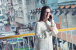 © Leo Zank - Young attractive caucasian brunette woman in eyeglasses standing on pedestrian footbridge and talking mobile phone. Blurred traditional Hong Kong street market as background.