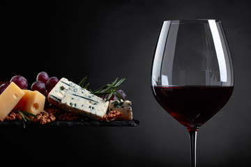 Glass of red wine with various cheeses , grapes and walnuts .