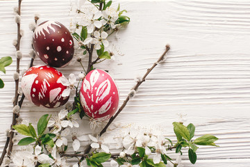 stylish painted easter eggs on rustic wooden background with spring flowers and willow branches. happy easter greeting card flat lay. space for text. modern colorful easter eggs