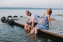 Happy Young Family Sitting On The Deck With Legs In Water Pregnant Woman Laughing