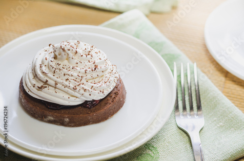 Zdjęcie XXL Ciasto czekoladowe z białą śmietaną na białym talerzu i widelcem, położone na zielonym serwetce