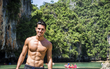 Half body shot of a handsome young man standing on a beach in Phuket Island, Thailand, shirtless wearing boxer shorts, showing muscular fit body