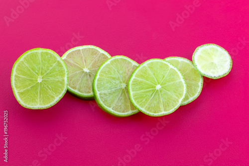 Slices Of Green Lemon Placed On Complementary Color Pink Background Slices Of Green Lemon Placed On Complementary Color Pink Background