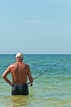 Bakc View Of A Senior, Male Wading, Relaxing And Surf Fishing In Tropical Water, Off A Beach On The Gulf Of Mexico