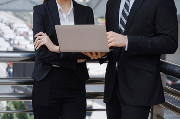 two business asian woman and caucasian man in suit talking and reading information about finance news in laptop computer in modern city, network technology, internet, successful and teamwork concept