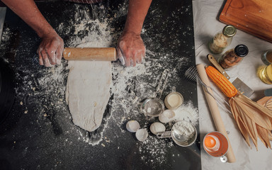 Wall Mural - Man preparing buns at table in bakery, Man sprinkling flour over fresh dough on kitchen table