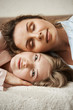 © Cookie Studio - Happy to find soulmate to share her thoughts. Vertical shot of attractive blonde girl lying on sofa with her girlfriend lying on her head, smiling broadly, feeling relaxed and cozy at home