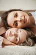 © Cookie Studio - Mother and daughter looking like best friends. Vertical shot of young attractive woman lying on head of another girl, looking at camera and smiling with relaxed and calm expression, feeling happy