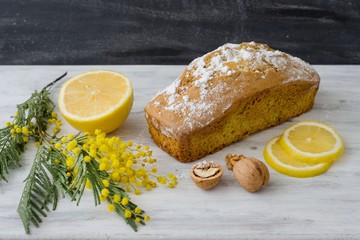 Lemon cake with nuts on a wooden white surface, a twig of mimosa flowers.