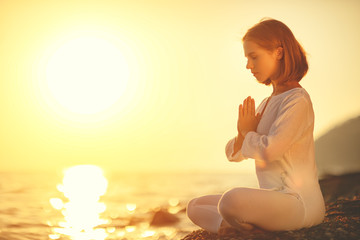 Wall Mural - woman practices yoga and meditates in lotus position on sunset beach.