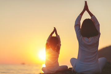 Happy family mother and child doing yoga, meditate in lotus position on beach