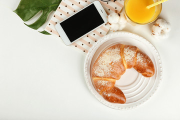 Wall Mural - Composition with fresh tasty crescent roll and mobile phone on white background