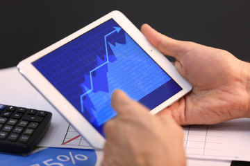 Man using tablet computer with stock chart data on screen at table. Forex concept