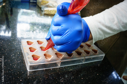 Fotografie, Obraz Chocolatier making candies, pouring into plastic mold