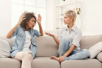 Two female friends sitting on sofa and arguing