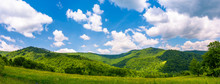 Panorama Of Beautiful Countryside In Summer. Beautiful Landscape With Forested Mountains And Grassy Field Under The Blue Sky With Some Clouds