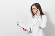 © ViDi Studio - Serious young doctor woman with stethoscope, glasses isolated on white background. Female doctor in medical gown talk on mobile phone, hold health card on notepad folder. Healthcare personnel concept.