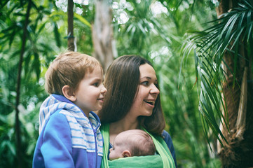 Wall Mural - A young mother with a baby in a sling and little boy is walking in the jungle