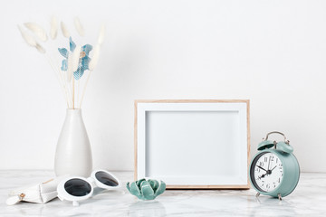 Poster frame mockup, front view, with decor elements and female accessories, flowers and blank copy space over the white wall.