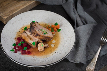 Wall Mural - Pork ribs with beets, carrots, fried mushrooms and sauce on a white plate. Restaurant serving. Old black rustic background. Top view