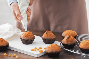 Sticker - Woman decorating tasty cupcakes with cream at table