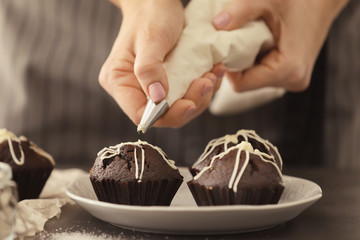 Sticker - Woman decorating tasty cupcake with frosting at table