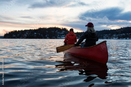 Cuadros en Lienzo Couple friends on a wooden canoe are paddling in an inlet surrounded by Canadian mountains during a vibrant sunset