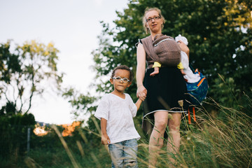 blonde caucasian mother with her two colored children are waiting hand in hand