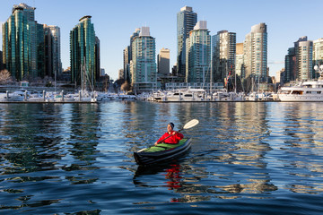 Man on an inflatable kayak is kayaking in Coal Harbour during a sunny morning. Taken in Downtown Vancouver, British Columbia, Canada.