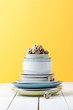 A stack of different tableware and quail eggs on a white wooden table near the yellow wall..