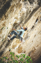Rock Climber Climbing Orange Limestone Wall Reaching Across For Handhold On Rock Face