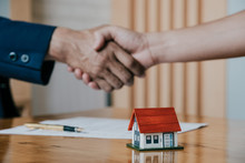 Estate Agent Shaking Hands With His Customer After Contract Signature, Contract Document And House Model On Wooden Desk