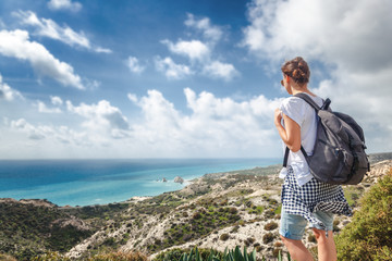 Wall Mural - a young traveler woman with a backpack on a stunning landscape background with the sea and green hills, traveling, hiking, together with nature, freedom and vacations concept