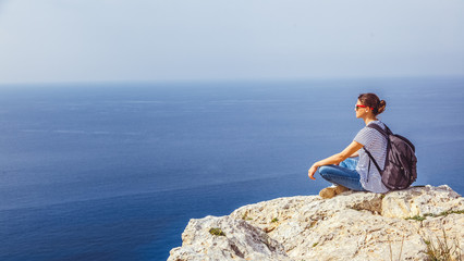 Wall Mural - A girl traveler sits on a rock and admires the blue boundless sea, freedom, travel, unity with nature,