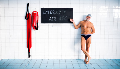 Wall Mural - Senior man standing in an indoor swimming pool.