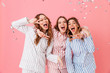 © Drobot Dean - Three happy women 20s wearing leisure clothings hugging and having fun at slumber party while showing victory sign, isolated over pink background