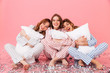 © Drobot Dean - Photo of happy women 20s wearing leisure clothings sitting barefoot on floor with legs crossed and hugging pillows during girlish sleepover, isolated over pink background