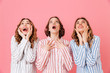 © Drobot Dean - Portrait of three joyful young girls 20s wearing colorful striped pajamas looking upward on copyspace with excitement during sleepover, isolated over pink background