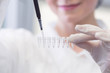 Close-up of female technician with multipipette and in genetic laboratory doing PCR research. Young woman is genetics scientist and she loads saliva samples for DNA amplification