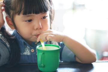 Wall Mural - asian children cute or kid girl thirsty and drinking cold water in green cup by tube for healthy and wear jean jecket with white space